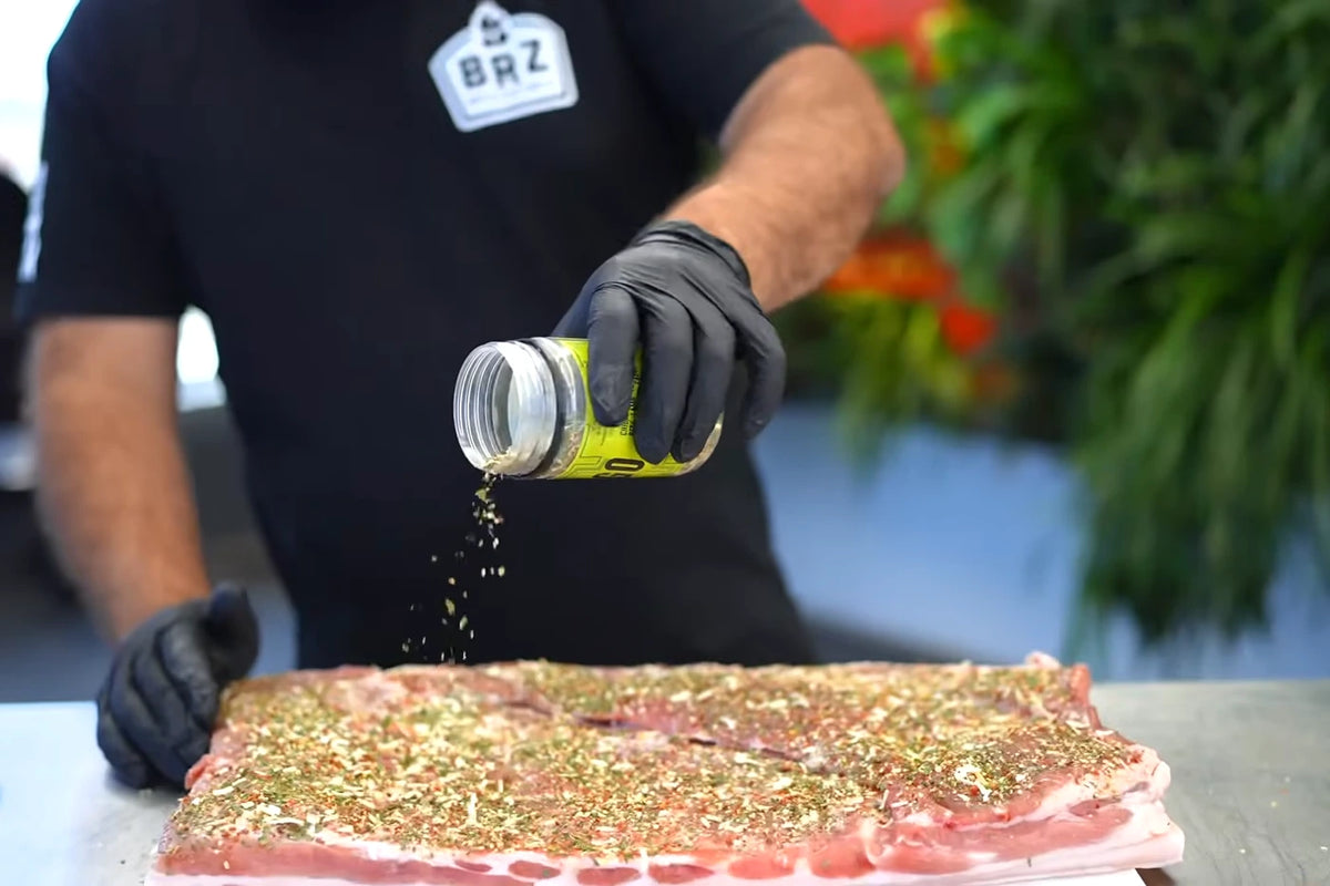 Gringo seasoning being sprinkled over pork belly before cooking