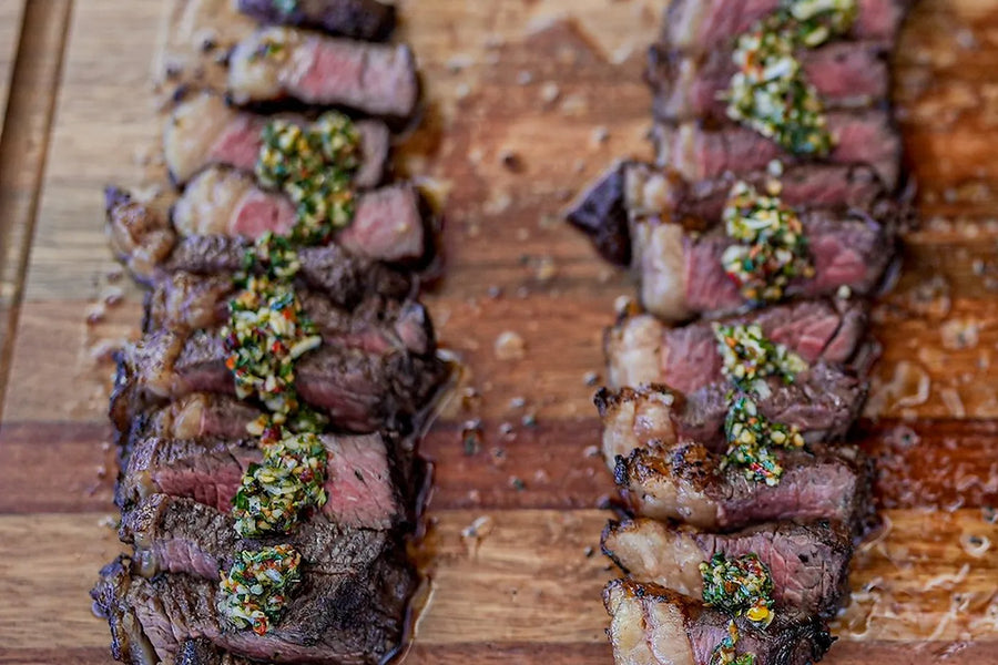 Two rump caps sliced across the grain on a timber board, pale fat showing along one edge of the slices, chimichurri spooned along the middle