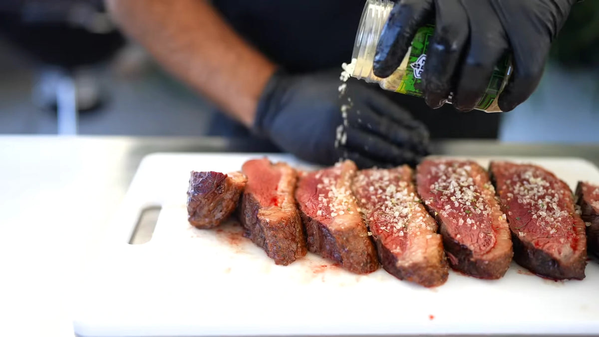 Picanha seasoning sprinkled from the jar over freshly sliced barbecue beef